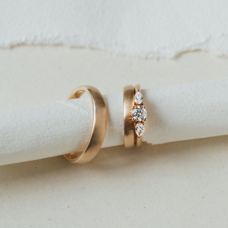 Drei goldene Ringe. Zwei Damenringe, bei denen ein klassischer Ehering mit einem Verlobungsring mit drei großen weißen Brillanten kombiniert wurde.