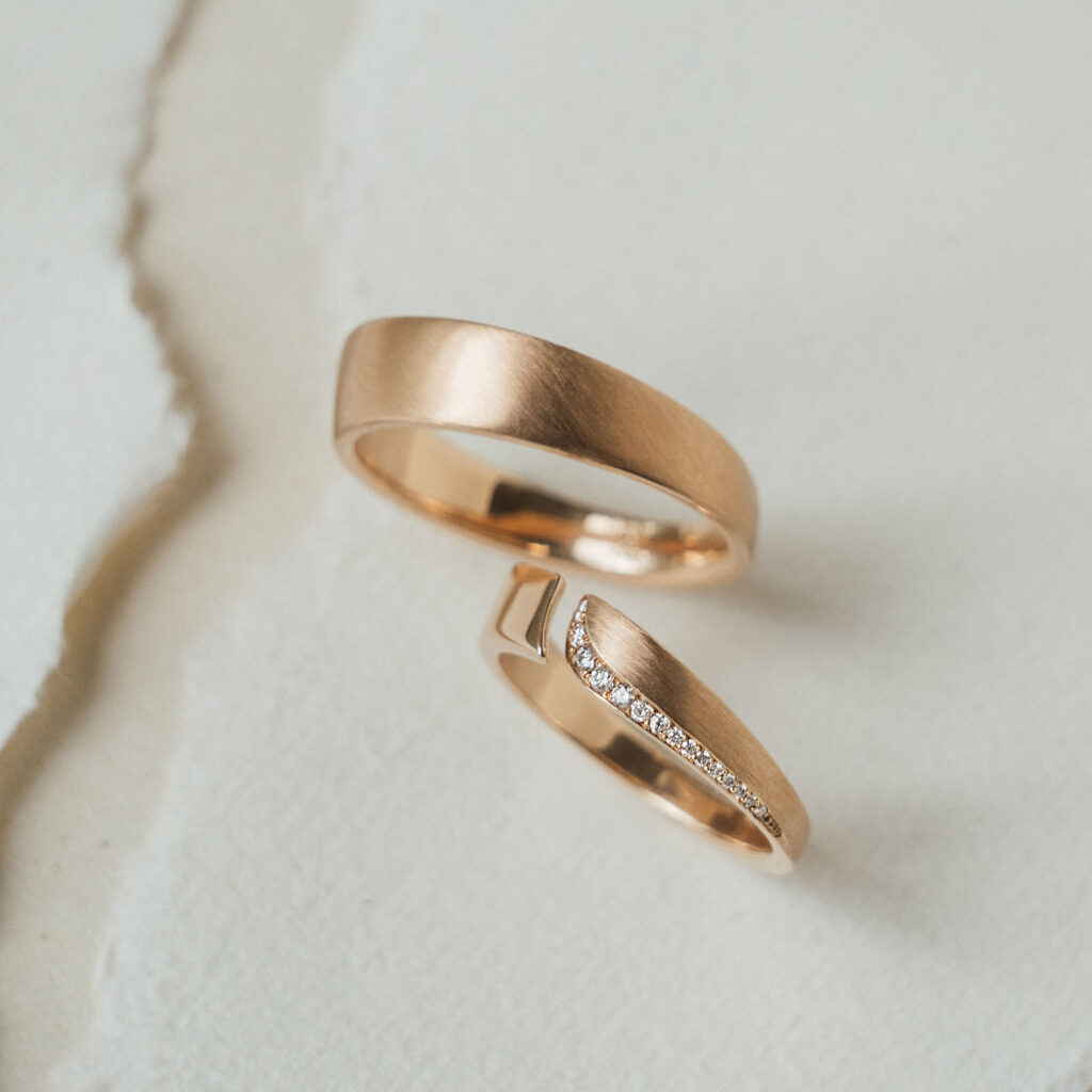 Eheringe in warmem Roségold, der Damenring mit Spalt und weißen Brillanten. Die Oberfläche matt