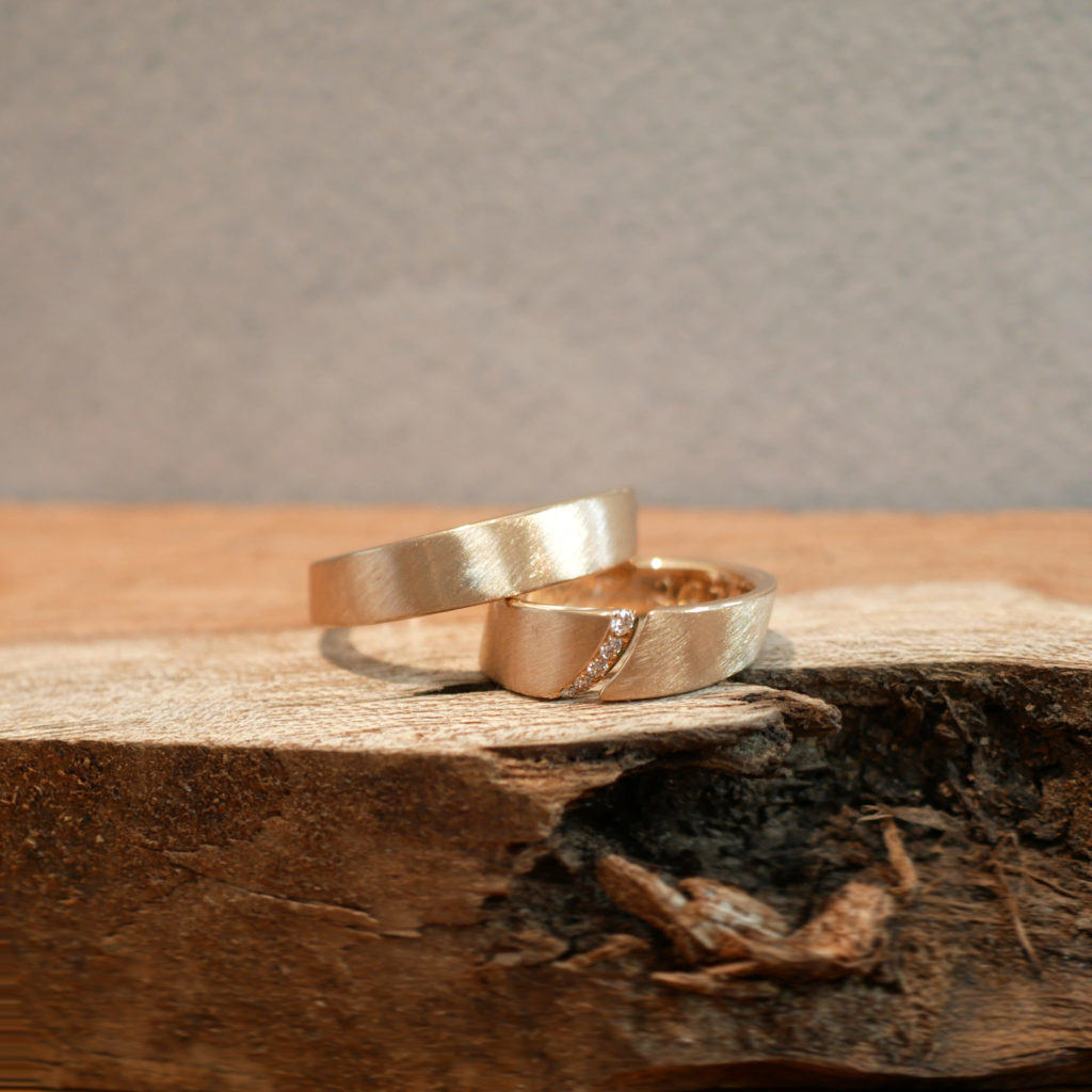 Bogenspalt Ring mit extravaganter Brillantreihe im Spalt. Die Trauringe werden präsentiert auf einem Holzstück.